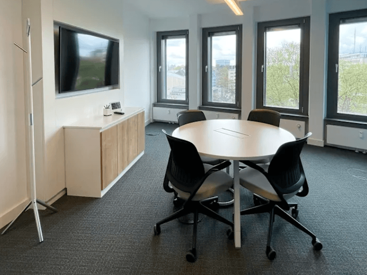 Kleiner Besprechungsraum mit Bürostühlen, Tisch und Monitor an der Wand
